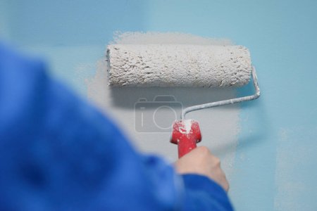 Close-up shot of a woman painting the wall of her house with a roller in a lighter color than the old one