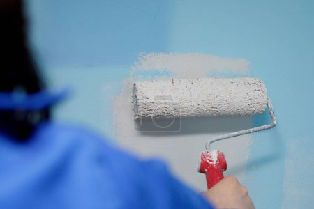 Gros plan d'une femme peignant le mur de sa maison avec un rouleau d'une couleur plus claire que l'ancien
