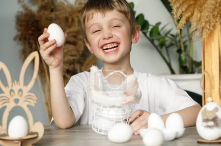Foto de A smiling child holds white eggs and an Easter basket with rabbit ears in his hands, symbols of the Easter holiday - Imagen libre de derechos
