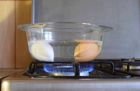 Téléchargez les photos : Faire bouillir les œufs dans une casserole en verre sur une cuisinière à gaz. - en image libre de droit
