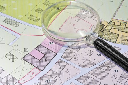 Photo for Imaginary cadastral map with buildings, land parcel and vacant plot - property registry and real estate concept seen through a magnifying glass - Royalty Free Image