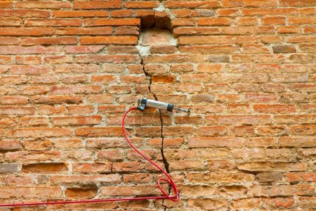 Electric digital crack measuring device reading, by cable, the minimal deformation and movement of a dangerous cracked brick wall