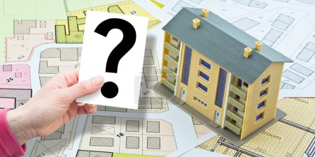 Photo for Doubts and uncertainties about buildings - concept with imaginary cadastral map and general urban plan with condominium residential building with and holding a card with question mark - Royalty Free Image