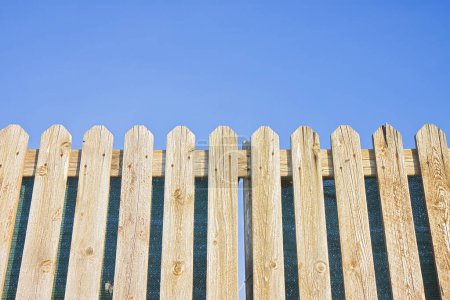 Téléchargez les photos : Détail d’une clôture en bois, construite avec des planches de bois hérissés contre un ciel bleu - en image libre de droit