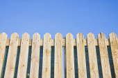 Detail of a wooden fence built with spiky wooden boards against a blue sky mug #690280740