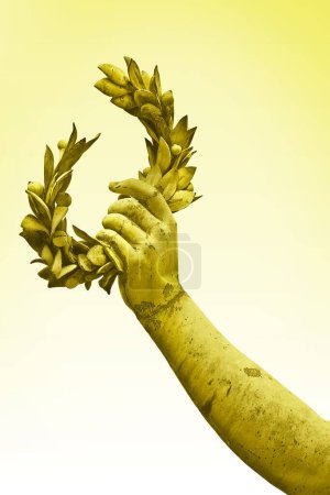 Mano sostiene una corona de laurel - estatua de bronce sobre fondo dorado - Imagen de concepto de éxito y fama