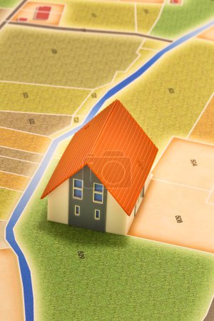 New home and free vacant land for building activity in rural land - Construction industry concept with a model of rural building and imaginary cadastral map 