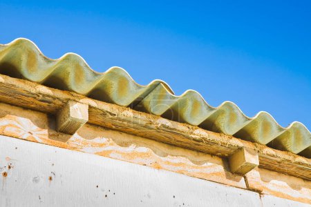 Altes und beschädigtes gefährliches Dach aus vorgefertigten und wellenförmigen Platten mit Holzstruktur - Asbestfasern können in die Luft freigesetzt und eingeatmet werden - sie verursachen Lungenkrebs