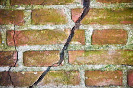 Muro de ladrillo agrietado expuesto viejo peligroso debido a la falla estructural de la fundación, hundimiento del suelo, corrosión y deterioro de materiales de construcción, terremoto 