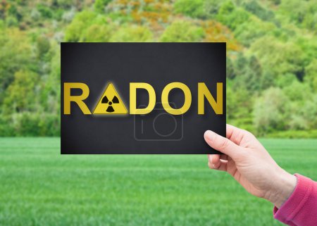 Foto de Alerta peligrosa Radon Gas - Concepto con la mano sosteniendo una postal contra un terreno baldío para la construcción residencial y la actividad de construcción - Imagen libre de derechos