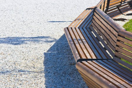 New bench with wooden slats and metal structure in a public park on white gravel pavement