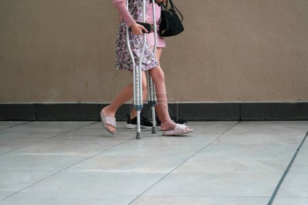 Téléchargez les photos : Fille marche avec des béquilles avec sa mère - en image libre de droit