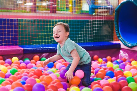 Feliz niño riendo en un centro de juegos de interior. Los niños que juegan con bolas de colores en la piscina de la bola del patio. Fiesta..