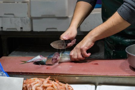 Großaufnahme männlicher Arbeiter beim Schneiden von Fisch mit Messer am Tisch.
