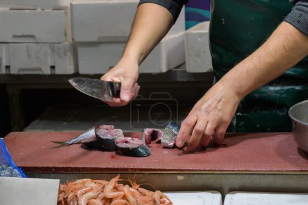Closeup of male workers hands cutting fish with knife at table.