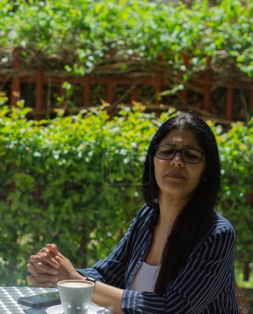 Téléchargez les photos : Jeune femme latine dans un café colombien, travaillant avec ordinateur portable et téléphone portable sur un après-midi ensoleillé - en image libre de droit