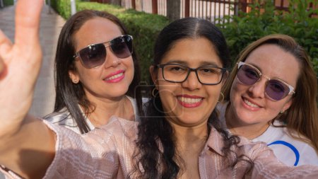Foto de Tres amigos tomando una selfie en verano con gafas y sonriendo mientras comparten - Imagen libre de derechos