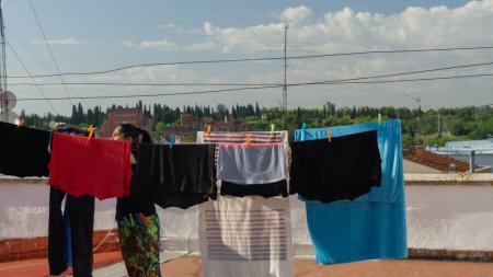 Foto de Joven latina mujer entre cuerdas colgando ropa en la azotea en verano - Imagen libre de derechos