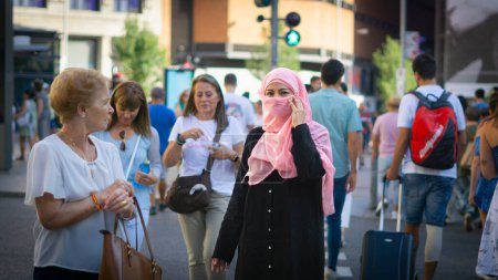 Foto de Mujer musulmana joven con velo en medio de la calle rodeada de gente - Imagen libre de derechos