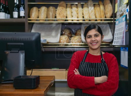 Foto de Joven empresaria sonriente con delantal y brazos cruzados junto a la caja registradora en la cafetería - Imagen libre de derechos