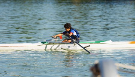 Foto de Niño de 10 años entrenando remo en un lago cerca de su casa con chaleco salvavidas azul en una tarde de verano. - Imagen libre de derechos