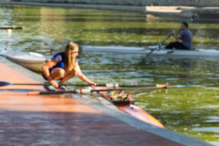 photo of rowing instructor in blur, preparing the boat for her student with boats around.