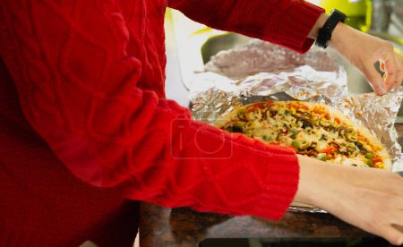 Photo for A woman in a red sweater is preparing a pizza in foil. She is adding toppings to the pizza - Royalty Free Image