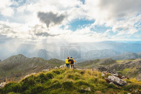 Téléchargez les photos : Couple de randonneurs avec sacs à dos, debout et embrassant sur le sommet d'une montagne contemplant le paysage de la chaîne de montagnes. sports et activités de plein air. - en image libre de droit