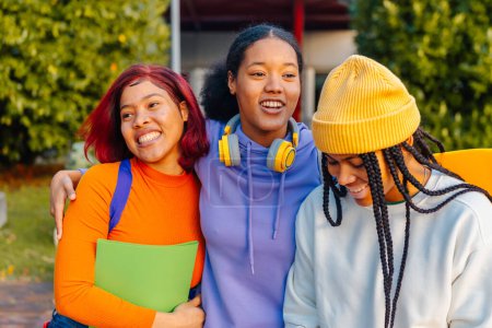 Foto de Grupo multirracial de tres adolescentes (latinas y negras) juntas a la salida de la escuela secundaria. amistad y unidad. cultura juvenil. piel sin retocar - Imagen libre de derechos
