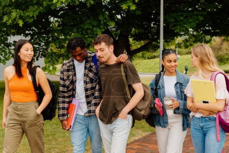 grupo multirracial y diverso de estudiantes caminando junto con útiles escolares y mochilas en las afueras del campus universitario o la escuela secundaria. de vuelta a la escuela.