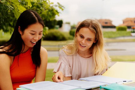 Photo for White girl and asian girl study together with notes sitting at a table outside the college or university campus. college lifestyle. classmates. - Royalty Free Image