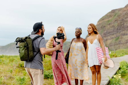 Foto de Fotógrafo y cineasta instruyendo a un grupo multirracial de modelos femeninas para grabar tomas en la playa al atardecer - Imagen libre de derechos
