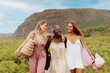 Téléchargez les photos : Portrait d'un groupe multiracial de jeunes femmes unies dans un geste d'amitié marchant ensemble sur une promenade sur la plage. Amitié et unité. - en image libre de droit