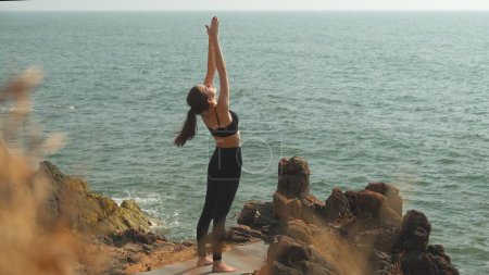 young woman is doing Urdhva Hastasana in Tadasana Mountain Pose by the ocean. High quality photo