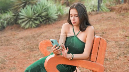 Photo for Young woman is looking at her phone while sitting in a chair in nature. High quality photo - Royalty Free Image