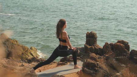 Photo for Young woman is doing Ashva Sanchalanasana on a seaside rocky shore. High quality photo - Royalty Free Image