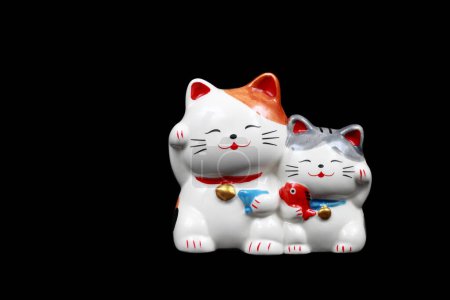 It is Two ceramic lucky cats for decoration isolated on black.