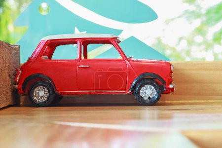It is Red car toy on wooden board.