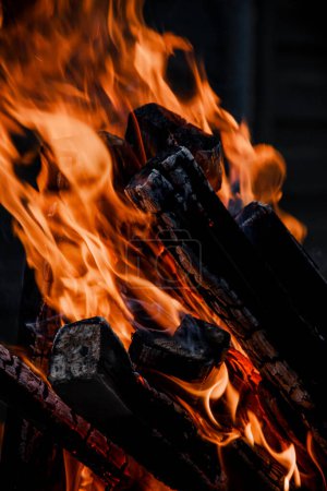 La photo montre un gros plan d'un feu flamboyant avec des flammes orange vif consommant des billes de bois. Le fond est sombre, ce qui met en évidence l'intensité du feu.