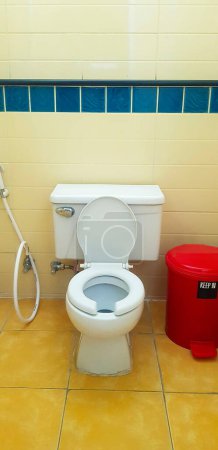 Toilettenspülung mit rotem Mülleimer auf gelber Fliese im Badezimmer, Toilette. Öffentlicher Waschraum und Reinraum. Design und keramisches Objekt