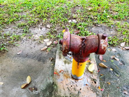 Old red fire hydrant connection for suppress or stop fire at public place with green grass. Rust object with copy space.