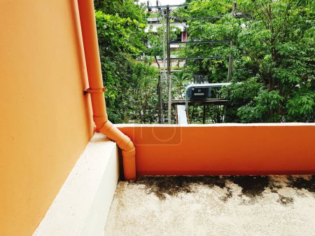 Téléchargez les photos : Balcon orange avec conduite d'eau ou tuyau d'évacuation à l'extérieur de la mezzanine avec transformateur et fond de plantes vertes. - en image libre de droit