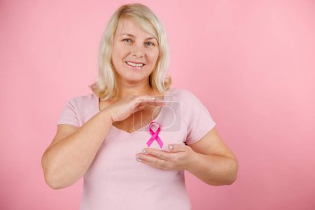 Foto de Mujer sosteniendo cinta rosa de cáncer apuntando con el pulgar hacia el costado sonriendo feliz con la boca abierta. Foto de alta calidad - Imagen libre de derechos