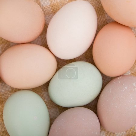 Huevos de diferentes colores en una canasta sobre fondo de lino. Vista de cerca desde arriba.