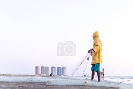 Photo for Karachi pakistan 2021, a fisherman wearing yellow jacket preparing fishing net for fishing at sea view in evening time. - Royalty Free Image