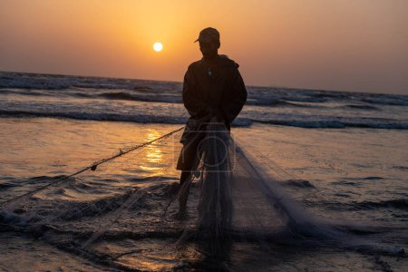 Téléchargez les photos : Karachi pakistan 2021, un pêcheur tirant un filet de pêche pour attraper du poisson, vue sur la mer en soirée. - en image libre de droit