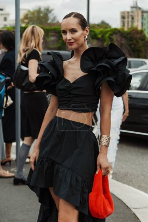 Téléchargez les photos : Un invité porte des boucles d'oreilles, un haut noir et une jupe, un sac rouge moelleux, vu à l'extérieur du défilé PRADA pendant la Fashion Week de Milan Vêtements Femme Printemps / Eté 2024. - en image libre de droit