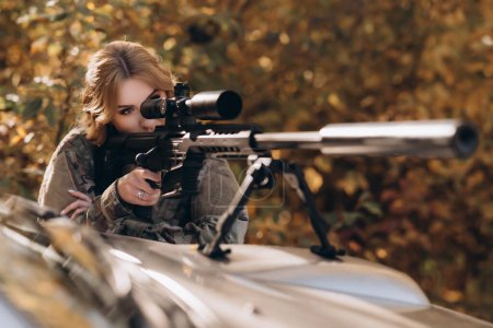 Téléchargez les photos : Une femme soldat tire un fusil depuis le capot d'une camionnette. Guerre, armée, concept militaire. - en image libre de droit