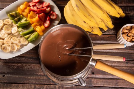 chocolate fondue accompanied by tropical fruits on wooden table and dark background