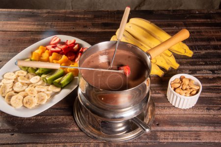 Foto de Fondue de chocolate acompañada de frutas tropicales sobre mesa de madera y fondo oscuro - Imagen libre de derechos